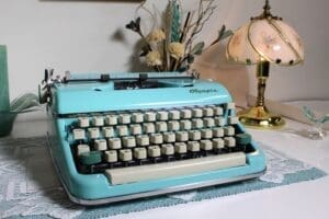 Olympia SM5 Typewriter in Teal Green on desk with Small brass lamp and dried flowers